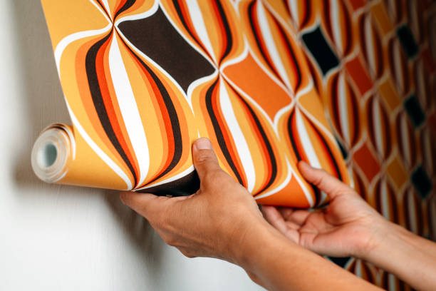 Roll of orange retro wallpaper being unrolled by hand